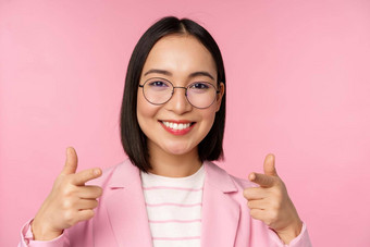 祝贺你微笑亚洲企业女人首席执行官经理西装眼镜指出手指相机招聘赞美赞美站粉红色的背景