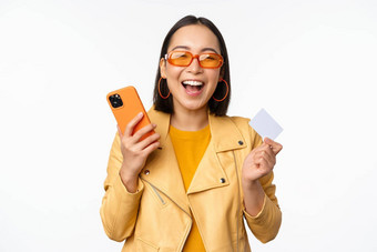 在线购物交付概念快乐朝鲜文女孩时尚的衣服持有信贷卡智能<strong>手机</strong>笑微笑站白色背景