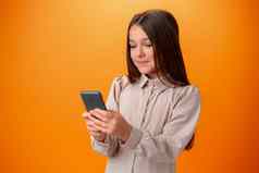 可爱的青少年女孩移动电话积极的表达式橙色背景