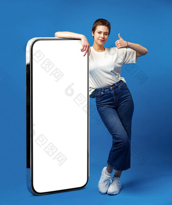 快乐年轻的女人倾斜巨大的手机空白色屏幕模拟