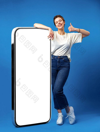 快乐年轻的女人倾斜巨大的手机空白色屏幕模拟