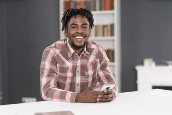 微笑英俊的非洲美国男人。智能手机检查社会媒体更新信息肖像年轻的男人。持有智能手机坐着表格社会媒体概念