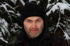 肖像英俊的旅行男人。穿黑色的针织他背景白雪覆盖的云杉分支机构