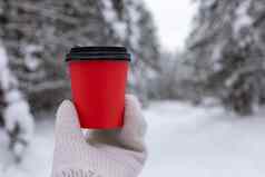 红色的纸杯咖啡手白色针织连指手套背景美丽的冬天森林