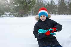 男孩坐在雪使雪球光蓝色的塑料雕刻工具