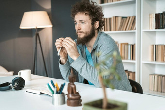 年轻的男人。工作<strong>首页</strong>远程沉思的窗口年轻的自由职业者男人。坐着桌子<strong>上</strong>移动PC<strong>首页</strong>办公室采取笔记工作<strong>首页</strong>概念