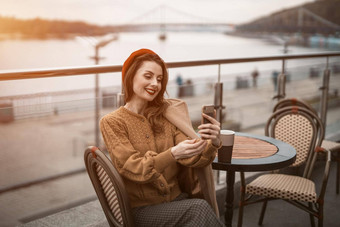 <strong>视频</strong>调用美丽的年轻的女人智能手机杯咖啡法国女人穿红色的贝雷帽坐着阳台餐厅咖啡馆背景秋天<strong>城市城市</strong>