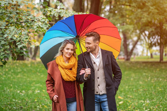 美丽的年轻的夫妇走公园彩虹彩色的伞美丽的女孩走秋天公园手臂手臂的家伙多雨的天气