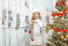 美丽的高加索人女孩精致的白色衣服冬天他持有条纹圣诞节袜子礼物装饰绿色圣诞节树圣诞节长袜