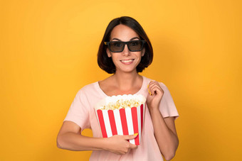 桶爆米花立体声眼镜手年轻的浅黑肤色的女人女人电影概念孤立的黄色的背景