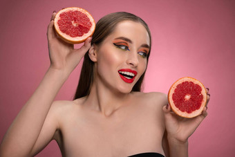 美丽的年轻的女人模型持有多汁的葡萄柚切片一半手横盘整理迷人的快乐的有趣的夫人红色的嘴唇长头发孤立的粉红色的背景