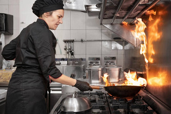 女人老板烹饪锅厨房烹饪燃烧的锅蔬菜商业厨房