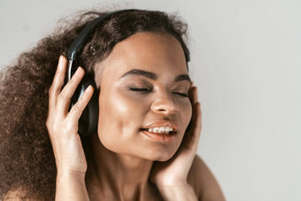 <strong>享</strong>受声音<strong>专</strong>业耳机年轻的非裔美国人女孩听音乐穿黑色的前孤立的灰色背景在情感上移动概念情绪面部表达式