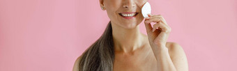 微笑灰色头发的亚洲女人清洗脸棉花垫站粉红色的背景