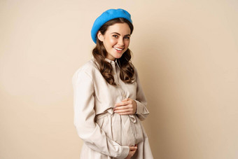 概念怀孕代孕年轻的温柔的温柔的女人大肚子微笑怀孕了女人摆姿势沟外套米色背景