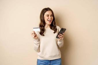 微笑女孩移动应用程序智能手机购物信贷卡站米色背景订单smth