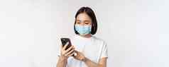 健康科维德概念年轻的亚洲女人医疗面具移动电话打字智能手机站白色背景