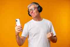 中间岁的男人。听音乐耳机智能手机黄色的背景