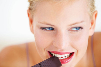 一点一点地吃颓废的治疗微笑年轻的女人享受美味的一块巧克力