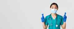 科维德冠状病毒疾病医疗保健工人概念兴奋充满希望的亚洲女医生护士医疗面具橡胶手套交叉手指好运气makign白色背景
