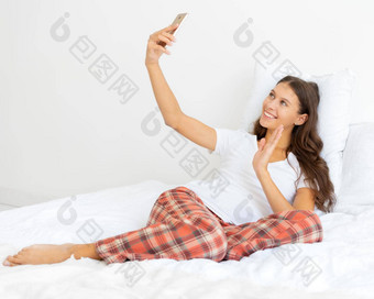 漂亮的女自拍金发女郎需要照片移动电话铺设床上挥舞着手