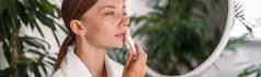 肖像年轻的女人美丽的脸应用唇乳香站浴室装饰植物
