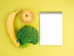 水果蔬菜苹果香蕉西兰花明亮的黄色的背景笔记本记录适当的营养维生素健康的生活方式