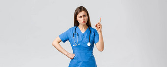 医疗工人医疗保健科维德疫苗接种概念皱着眉头年轻的女护士医生蓝色的实习医生风云皱着眉头摇晃手指责骂病人坏行为灰色背景