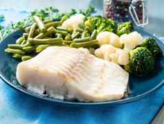 烤海鱼鳕鱼角蔬菜蓝色的板蓝色的餐巾一边视图健康的饮食