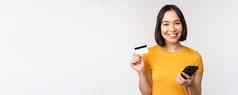 美丽的微笑亚洲女孩信贷卡移动电话支付在线智能手机站黄色的T恤白色背景