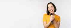 快乐亚洲女孩唱歌有趣的持有麦克风卡拉ok站黄色的T恤白色背景