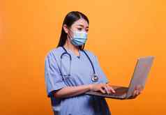 年轻的成人护士穿病毒保护口罩听诊器移动PC