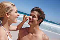 爱保持安全防晒霜拍摄快乐年轻的女人应用防晒霜男朋友鼻子海滩