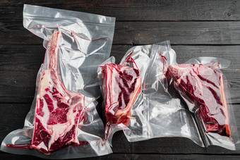 干岁的牛排真空肉产品塑料包战斧骨俱乐部牛排削减黑色的木表格背景