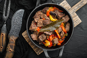 牛肉肉红烧土豆胡萝卜香料投铁煎锅黑色的石头背景前视图平躺