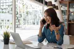 快乐年轻的亚洲女人会说话的移动电话微笑坐着工作移动PC文书工作办公室
