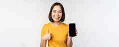 技术人概念微笑年轻的女人显示拇指智能手机屏幕移动电话应用程序接口站白色背景