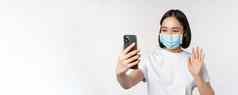 健康科维德概念现代亚洲女孩学生医疗面具视频闲谈，聊天移动电话挥舞着手智能手机应用程序站白色背景