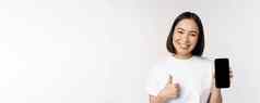 肖像美丽的亚洲女人显示拇指智能手机屏幕微笑广告移动电话应用程序白色背景