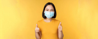微笑亚洲女人医疗脸面具显示拇指批准<strong>推荐</strong>smth站黄色的背景