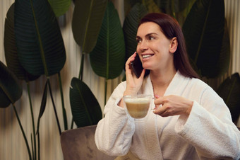 美丽的女人持有杯卡布奇诺咖啡咖啡喝会说话的电话放松水疗中心休息室接收振兴抗衰老治疗美容水疗中心概念