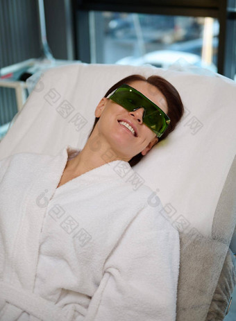 有吸引力的自信欧洲女人女病人保护眼镜穿<strong>白色</strong>特里<strong>浴袍</strong>说谎按摩沙发上健康身体护理程序现代水疗中心诊所