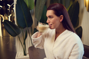一边肖像优雅的美丽的黑暗头发的中间岁的女人白色特里浴袍喝卡布奇诺咖啡咖啡打破放松水疗中心专业美治疗美容概念