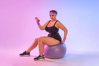 大小健身模型运动教练教练女人首页健身房坐健身球孤立的粉红色的背景锻炼体育运动概念