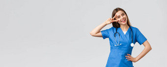 医疗工人医疗保健科维德疫苗接种概念快乐的有吸引力的女护士医生蓝色的实习医生风云听诊器显示和平标志保持乐观站灰色背景