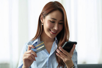 年轻的美丽的亚洲女人智能手机信贷卡在线购物首页复制空间网络支付技术购物狂生活方式移动电话<strong>金融</strong>应用<strong>程序</strong>概念