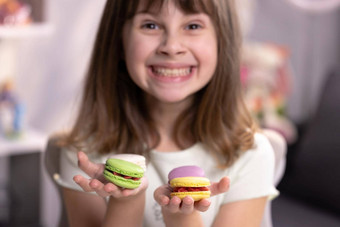 微笑可爱的学校孩子女孩持有美味的饼干手相机传统的法国五彩缤纷的蛋白杏仁饼干食物概念