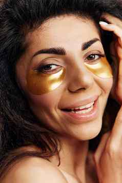 享受漂亮的卷曲的拉丁夫人黄金水凝胶补丁眼睛持有手头发摆姿势孤立的黄色的背景化妆品产品自然美概念工作室特写镜头肖像