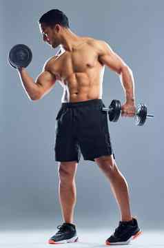 目标使肌肉工作室拍摄肌肉发达的年轻的男人。锻炼哑铃灰色背景