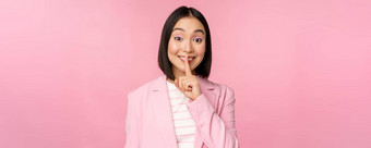 嘘禁忌概念肖像亚洲女商人显示嘘手势嘘标志新闻手指嘴唇站粉红色的背景西装